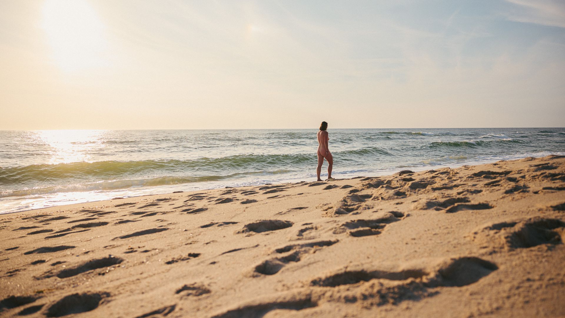 Person spaziert am sonnigen FKK-Strand von Sylt entlang.