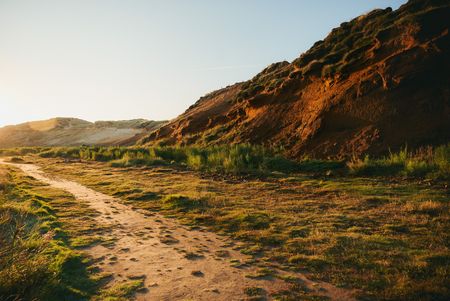 Sandiger Pfad neben den rötlichen Klippen des Morsum Kliffs, beleuchtet von der Abendsonne.