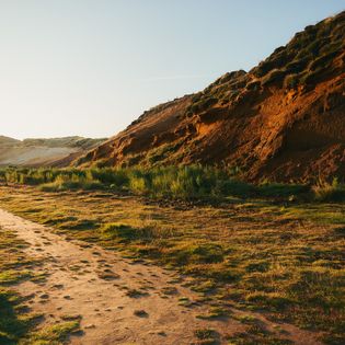 Sandiger Pfad neben den rötlichen Klippen des Morsum Kliffs, beleuchtet von der Abendsonne.