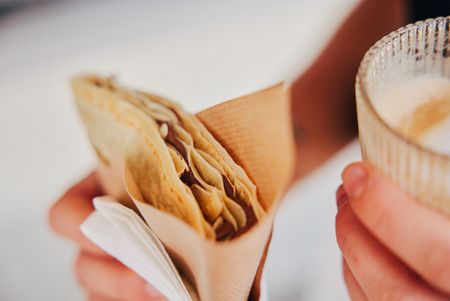 Crêpe mit Schokolade und Glas Kaffee in den Händen gehalten.