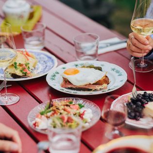 Verschiedene Speisen, darunter Käse, Kartoffeln und Brot, auf einem rot lackierten Tisch im Käseklub in Keitum auf Sylt, mit Gläsern Wein und Wasser.