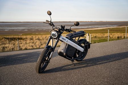 Ein moderner E-Roller der Marke "Island Riders" steht auf einer Straße vor einer Küstenlandschaft. Der Roller ist schwarz-weiß und hat breite Reifen.