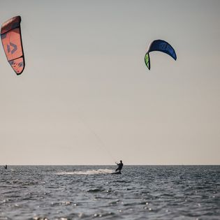 Zwei Kitesurfer mit bunten Kites auf der Nordsee vor klarem Horizont.