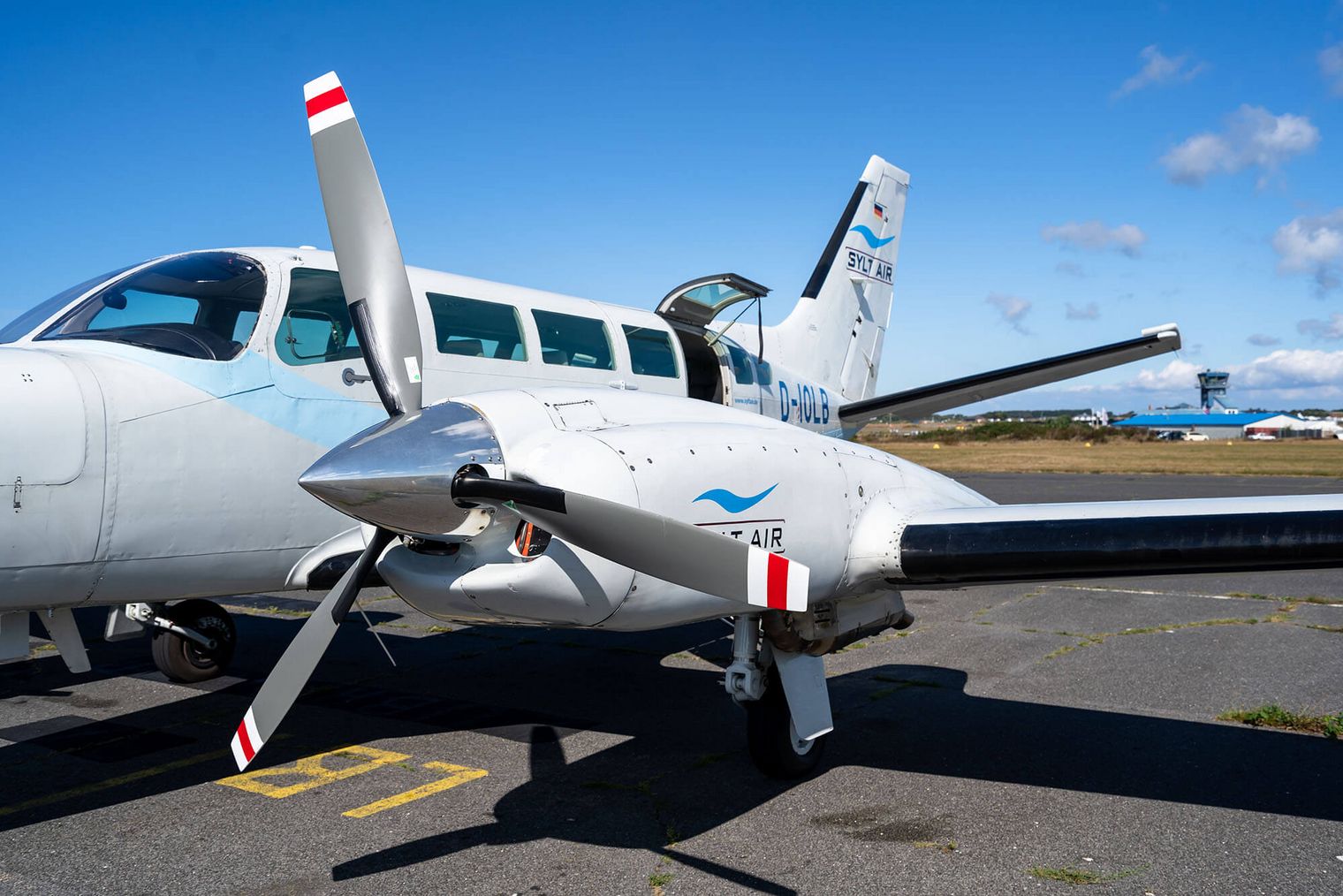 Ein kleines Passagierflugzeug der Sylt Air vom Typ Cessna 404 steht auf einem Flugfeld unter blauem Himmel.