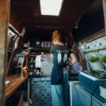 Barista bereitet Kaffee in einem stilvollen Kaffeebus mit Holzelementen und Fliesenoptik zu.