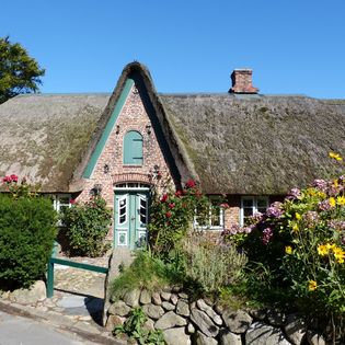 Historisches Reetdachhaus mit buntem Blumenbeet und Steinmauer in Keitum.