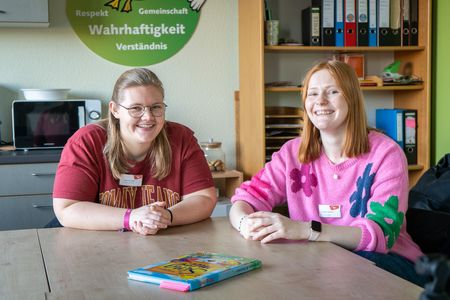 Jannika Kasten und Antonia Stoll sitzen nebeneinander im Büro und schauen in die Kamera.