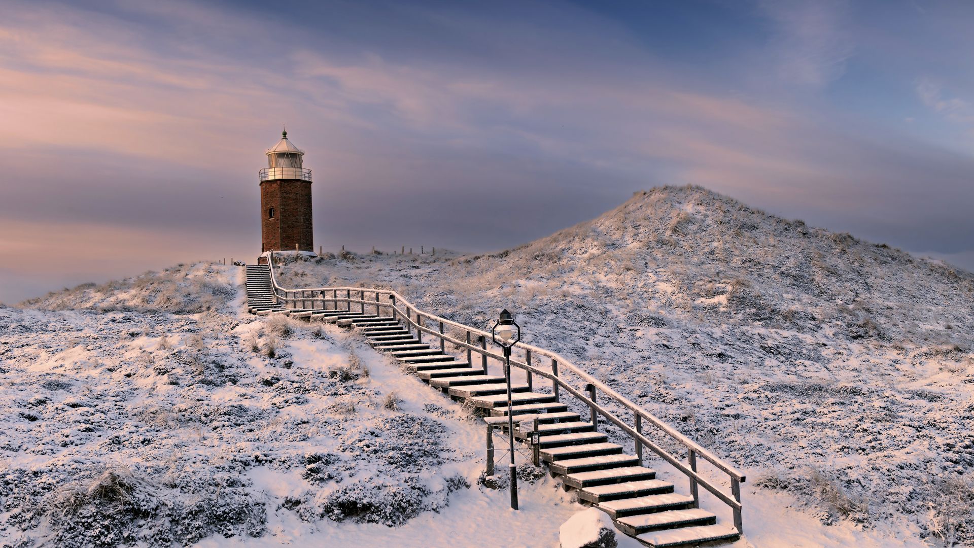 Kampener Leuchtfeuer auf schneebedeckten Dünen unter einem bunten Abendhimmel.