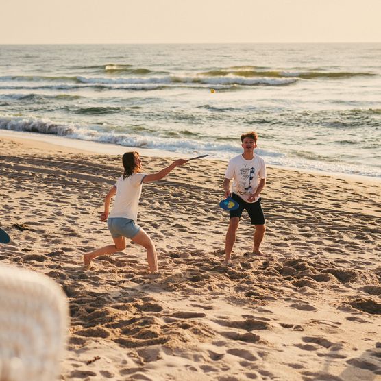 Vier Personen spielen Strandtennis im Abendlicht vor der Nordsee.