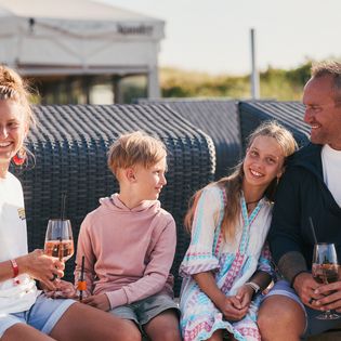 Familie mit zwei Kindern sitzt lachend auf einer Terrasse und genießt die Zeit zusammen.