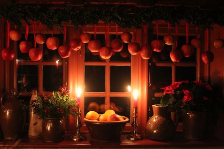 Weihnachtlich dekoriertes Fenster mit hängenden roten Äpfeln, Kerzen und Töpfen mit weihnachtlichen Dekorationen.