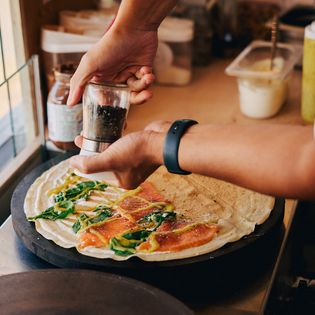 Person würzt Crêpe mit Lachs und Kräutern auf heißer Platte.