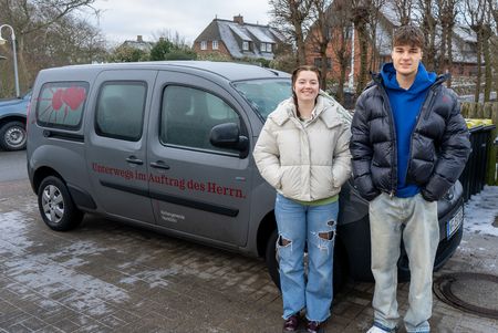 Zwei junge Menschen stehen vor dem Auto der Norddörfer Kirchengemeinde.