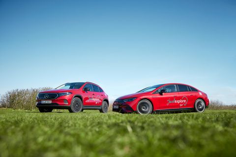 Zwei rote Mercedes-Fahrzeuge mit dem Schriftzug "just explore Sylt" stehen auf einer Wiese unter einem blauen Himmel. Links ein SUV, rechts eine Limousine.