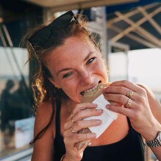 Frau beißt in einen Snack, Hintergrund mit Sonnenschirmen.