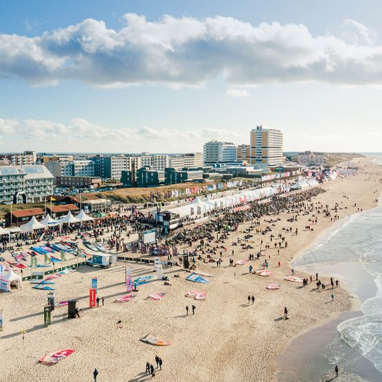 Der Windsurf World Cup auf Sylt mit weißen Zelten entlang der Promenade, Menschen am Strand und der Skyline von Westerland im Hintergrund.