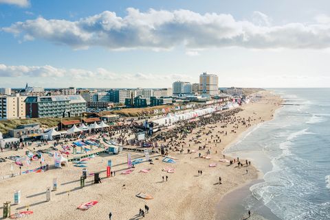 Der Windsurf World Cup auf Sylt mit weißen Zelten entlang der Promenade, Menschen am Strand und der Skyline von Westerland im Hintergrund.