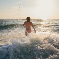 Frau läuft ins Meer bei goldenem Sonnenuntergang. 