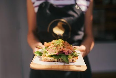 Sauerteigbrot mit Lachs, Spinat und Avocado auf einem Holzbrett präsentiert.