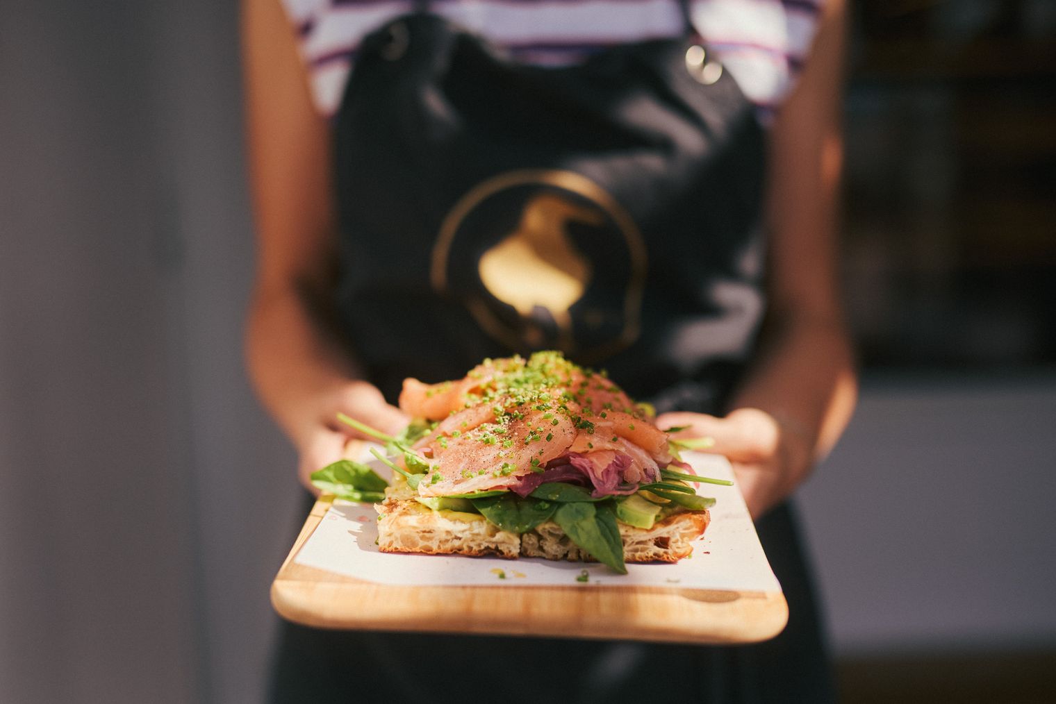 Sauerteigbrot mit Lachs, Spinat und Avocado auf einem Holzbrett präsentiert.