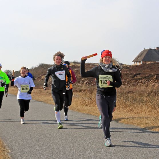 Gruppe von Läufern bei einem Staffellauf des Syltlaufs auf einem Naturweg, vorderste Frau hält den Staffelstab.