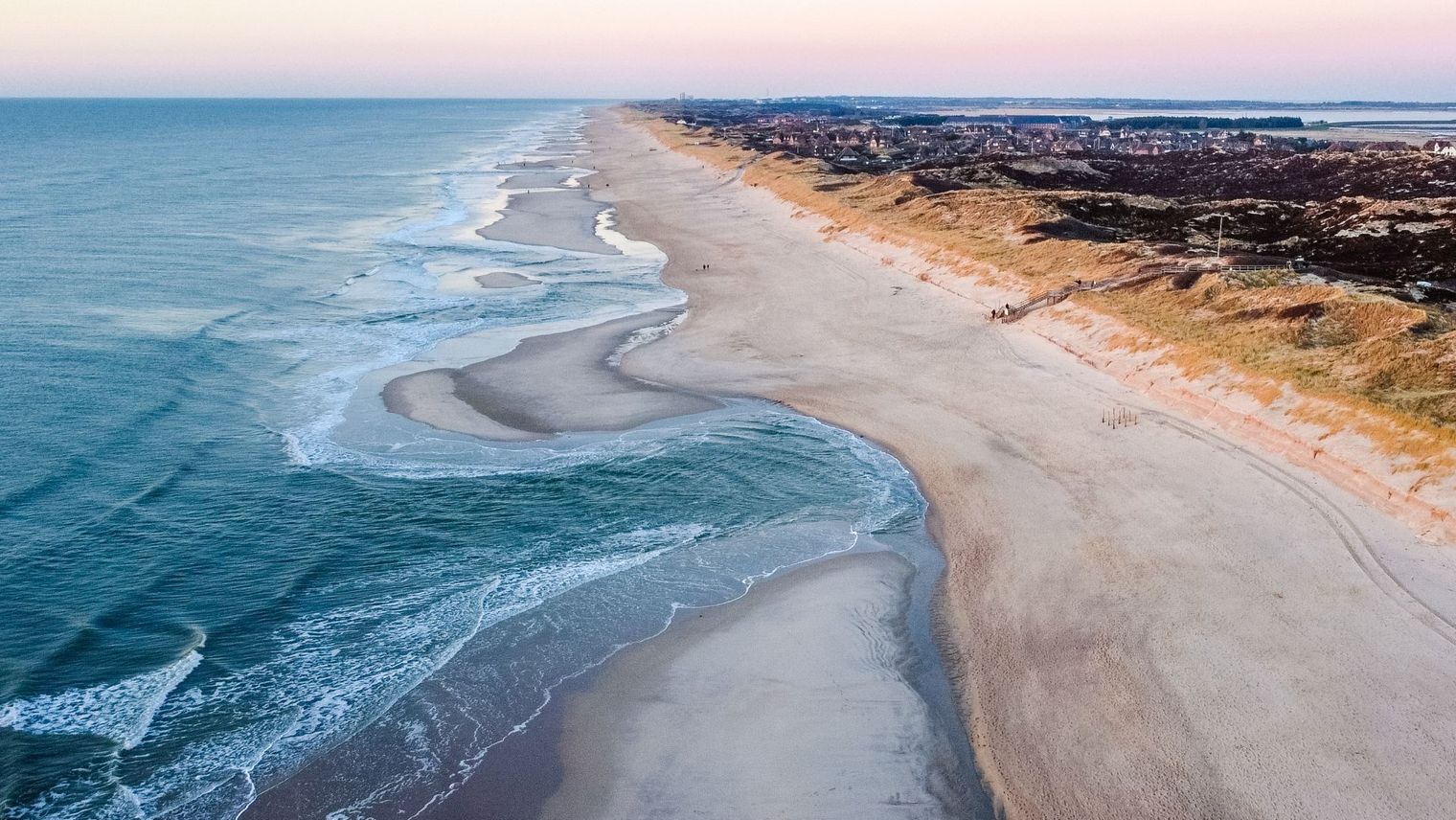 Ein Blick auf den kilometerlangen Sandstrand von Sylt aus der Vogelperspektive. Die Dünenlandschaft und das klare blaue Meer sind Natur pur. 