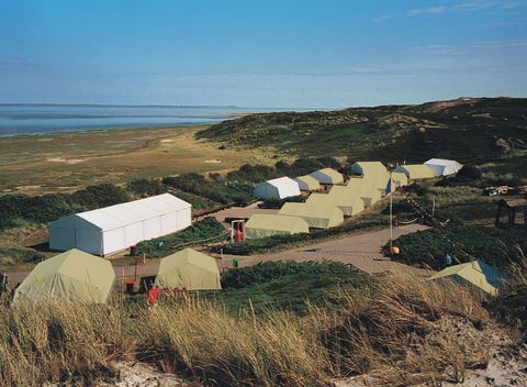 Der Jugendzeltplatz Strandlaeufernest auf Sylt mit mehreren Zelten und einem Hauptgebäude, eingebettet in die Dünenlandschaft.