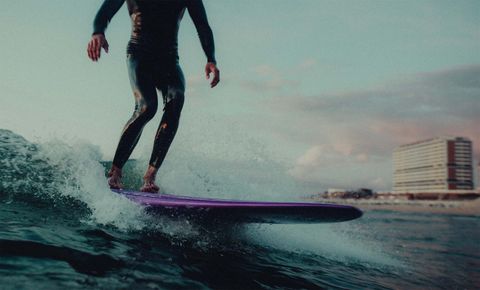 Ein Surfer mit einem lilanen Surfboard im Wasser 