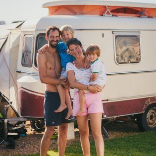 Eine Familie mit zwei Kindern posiert vor ihrem Wohnwagen in der Sonne.