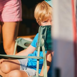 Ein Junge schaut neugierig hervor, während er auf einem Campingstuhl sitzt.