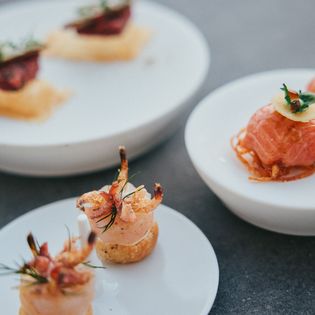 Häppchen aus Meeresfrüchten, Lachs und knusprigen Toppings auf weißen Tellern.