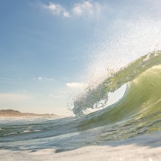 Brechende grüne Welle vor klarem Himmel und Küste.