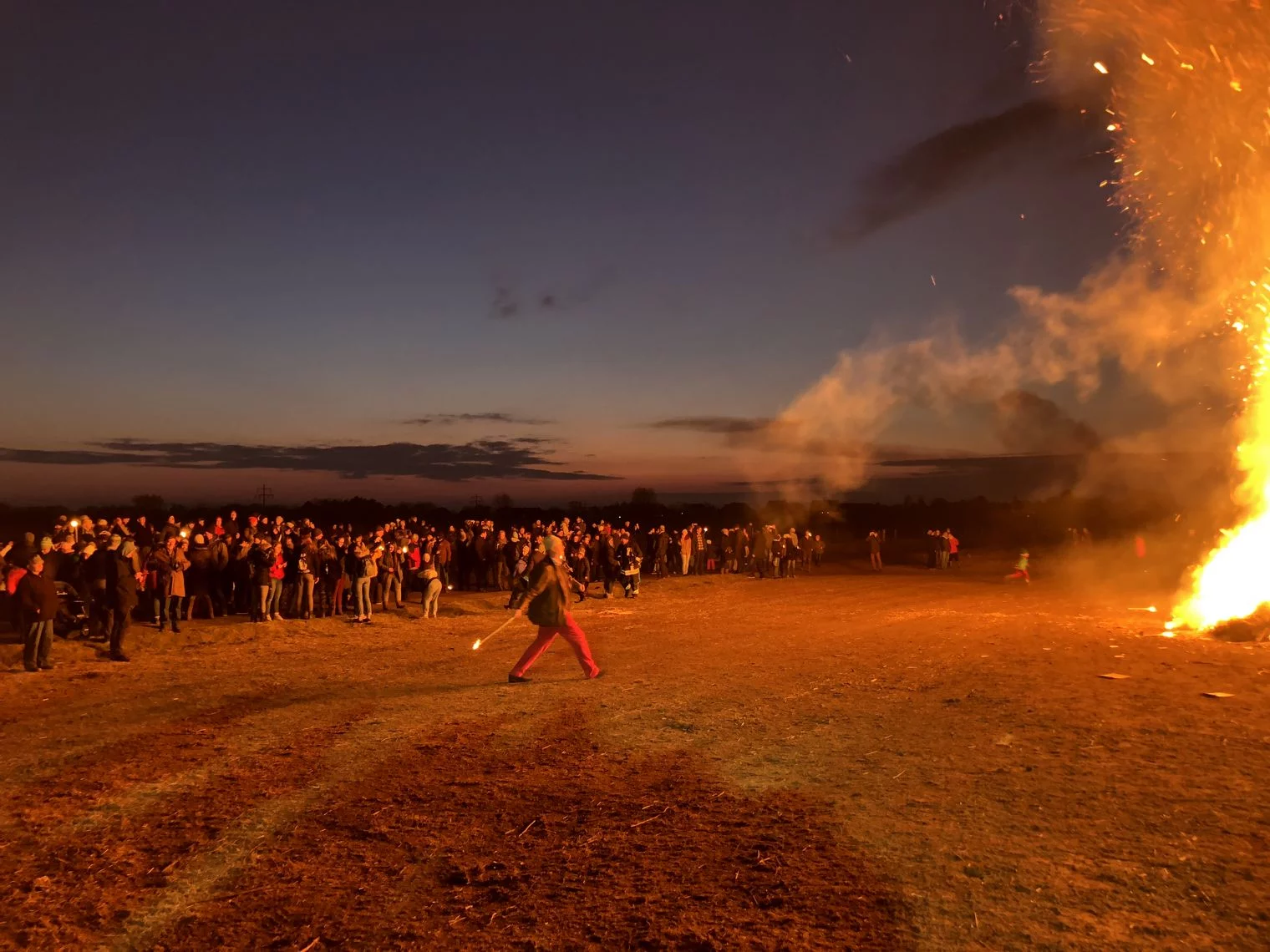 Menschen werfen Fackeln in ein großes Feuer beim Biikebrennen in der Dämmerung.