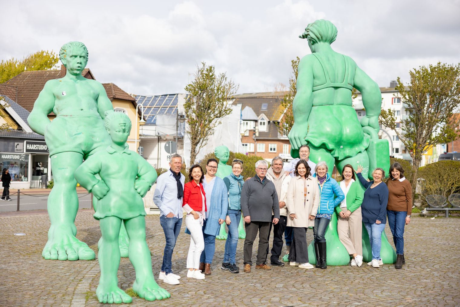 Gruppe von Menschen der Sylter Gästeführer:innen vor den grünen Skulpturen "Reisende Riesen" auf dem Vorplatz des Bahnhofs in Westerland.