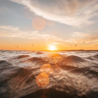 Wellen im Vordergrund, Kites und Sonnenuntergang am Horizont.