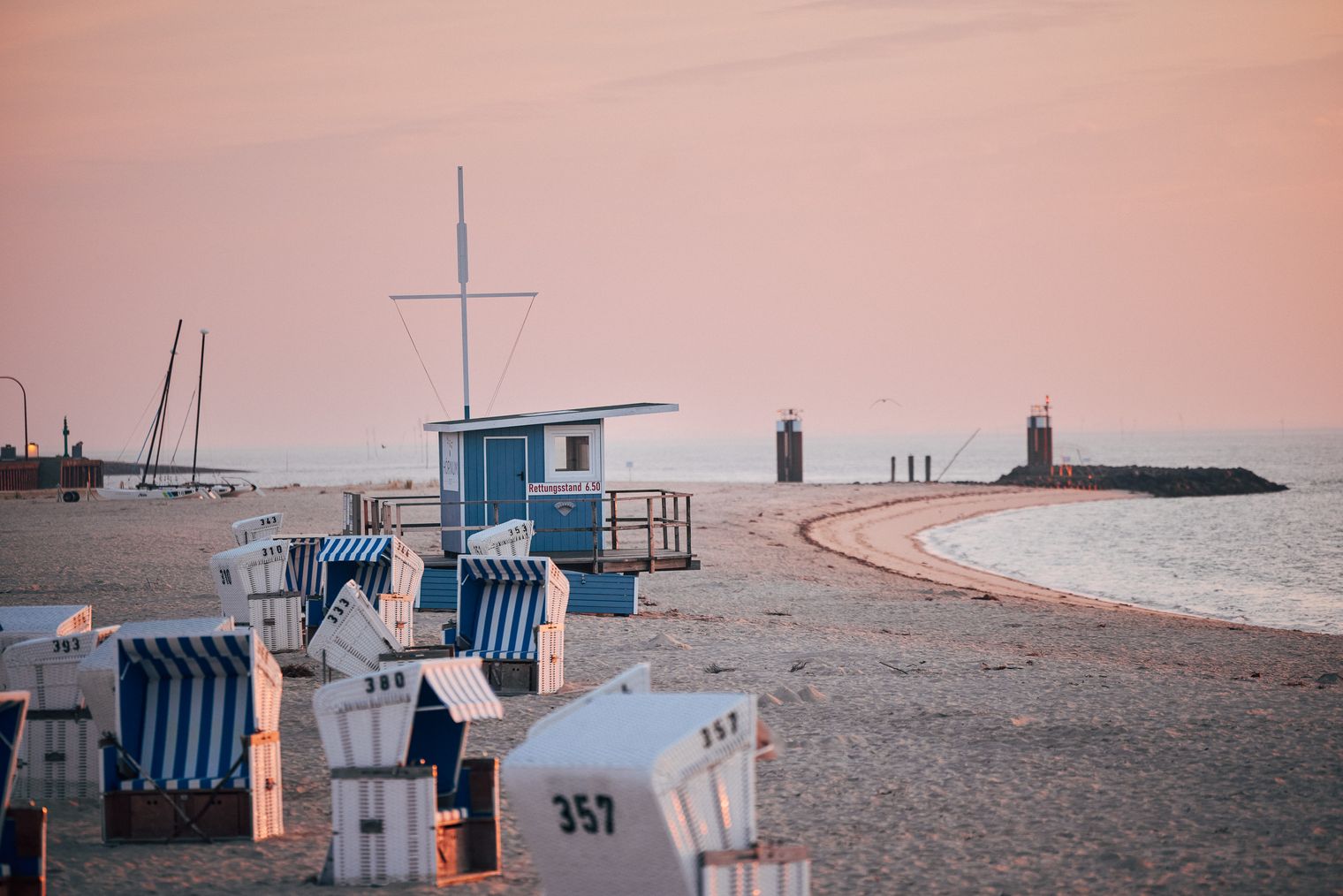 Strandkörbe und ein blauer Rettungsstand am Strand von Hörnum bei Sonnenuntergang, mit einer geschwungenen Küstenlinie und der Nordsee im Hintergrund.