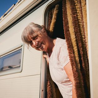 Eine ältere Frau schaut aus dem Fenster eines Wohnmobils, umgeben von bunten Vorhängen