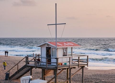 Erhöhte Rettungsstation am Strand, umgeben von Strandkörben, mit Wellen und Abendhimmel im Hintergrund