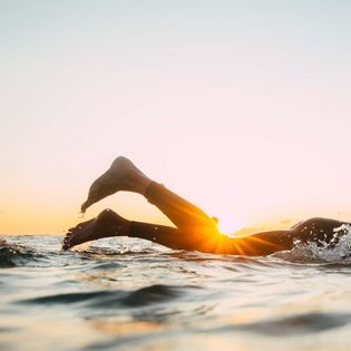 Beine eines Schwimmers im Wasser vor Sonnenuntergang.